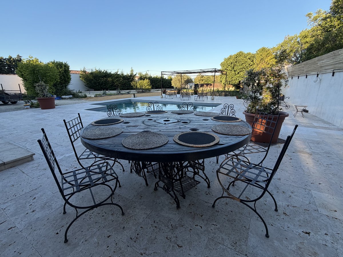 Table ronde en fer forgé avec chaises, terrasse travertin et piscine – Villa Jeff